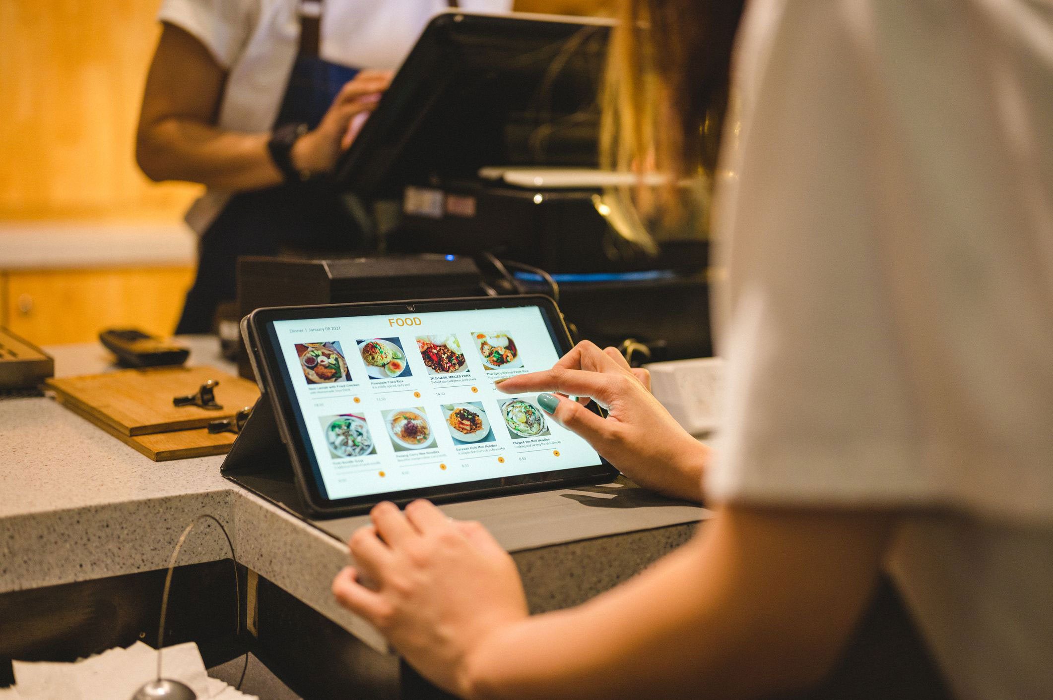 Mulher em frente a um balcão de atendimento de um restaurante selecionando os pratos em um cardápio digital de tablet.