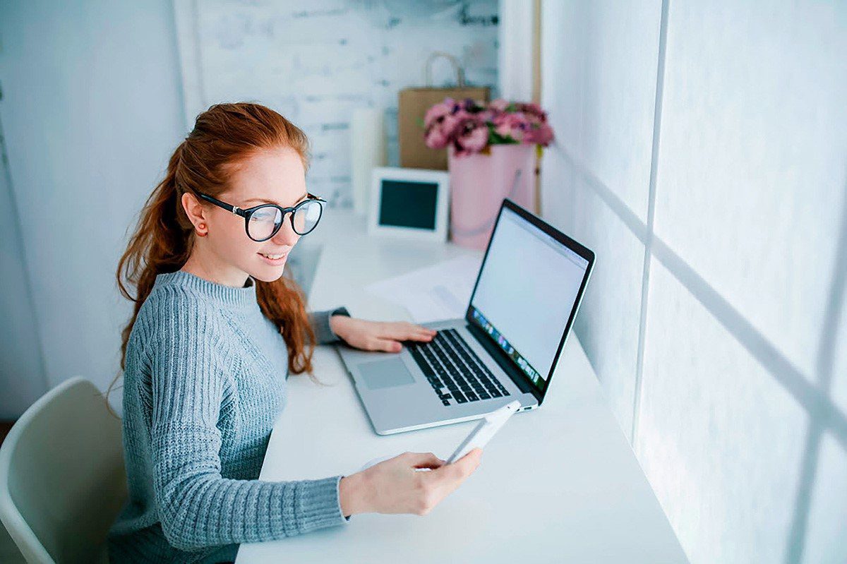 Mulher ruiva no escritório trabalhando através do celular e notebook